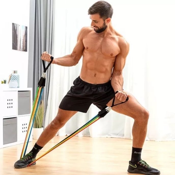 homme tire elastique musculation en position fente laterale elastique tenu par les deux mains et passe sous son pied dans salon