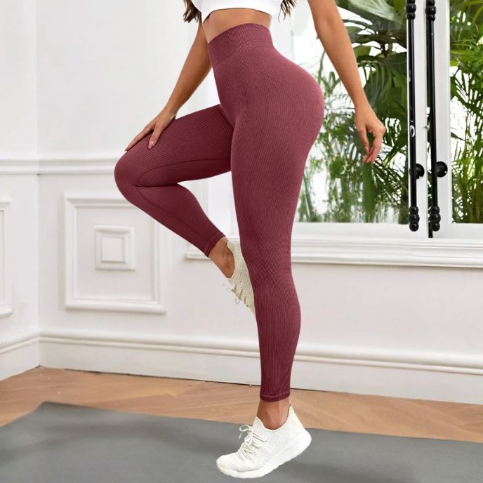 femme porte legging sport de couleur rouge vin vue de côté dans sa chambre
