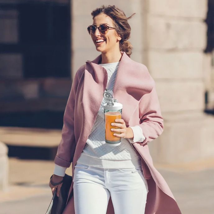 femme avec manteau rose porte shaker proteine powershake Ă la main