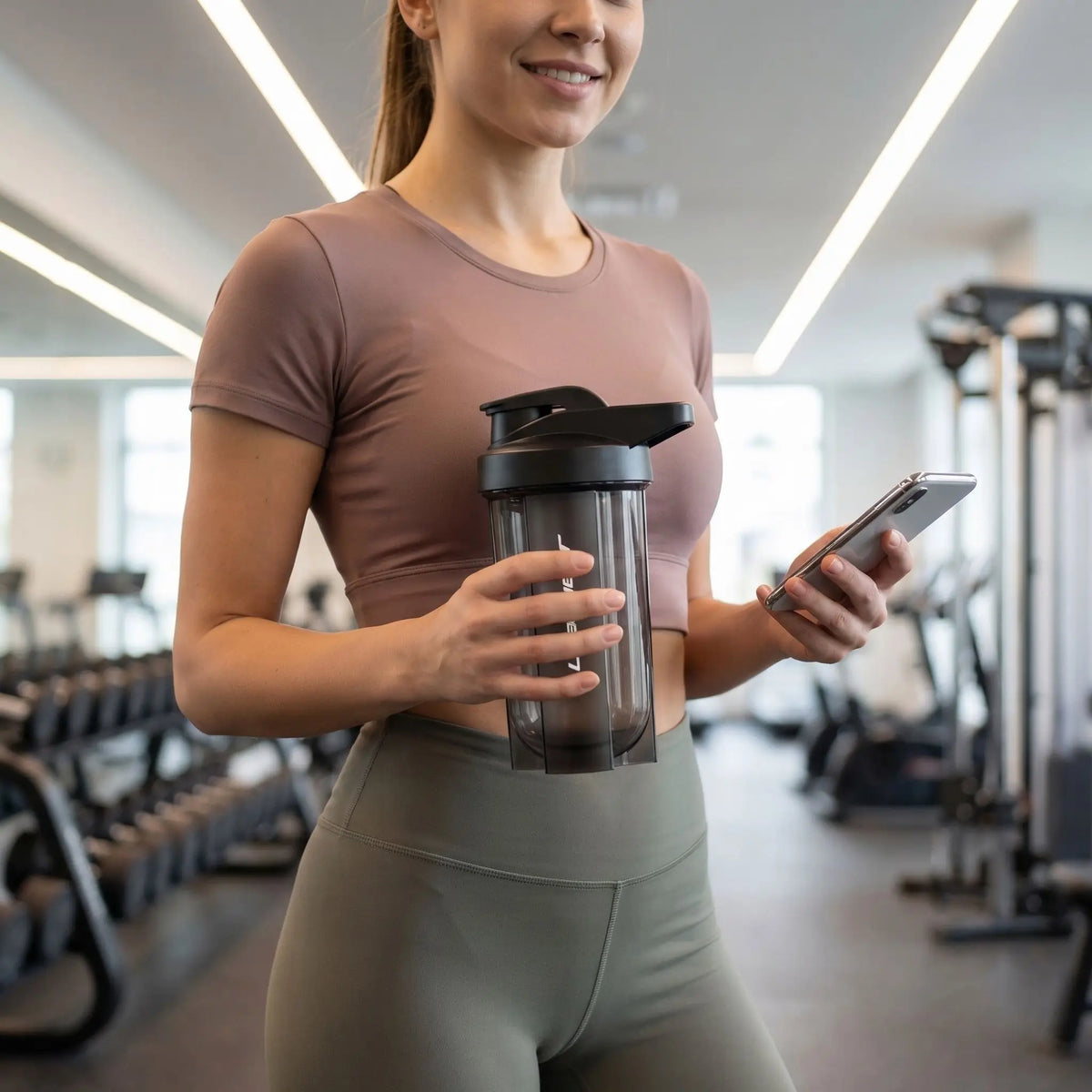 femme tient shaker noir dans une salle de fitness