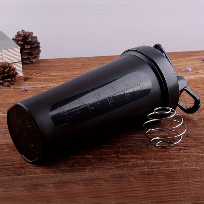 Shaker noir avec boule mélangeuse en métal posé sur une table en bois