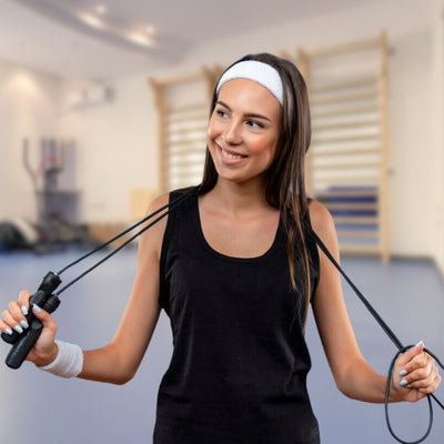 femme tient corde a sauter noire autour de son cou dans une salle fitness
