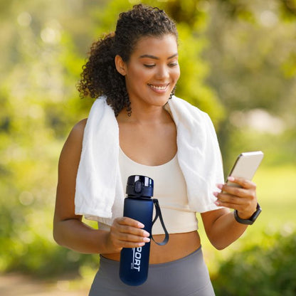 femme tient gourde de sport bleu à la main et téléphone mobile a l autre main