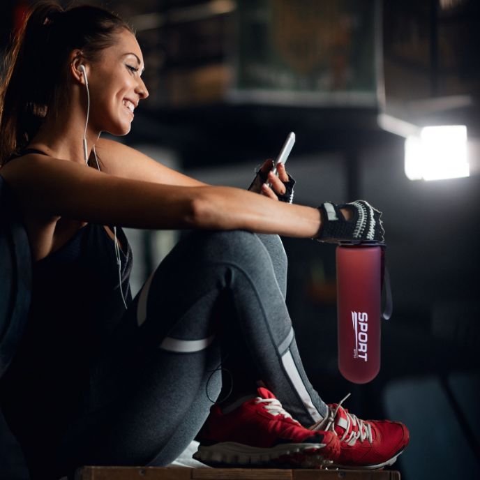 femme assise tient gourde de sport rouge à la main dans une salle de fitness