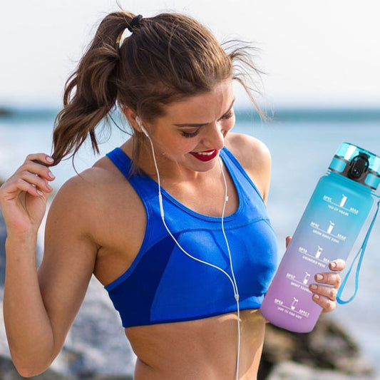 Jeune femme en brassière de sport et écouteurs utilisant sa gourde pour le sport pendant une pause entraînement en plein air