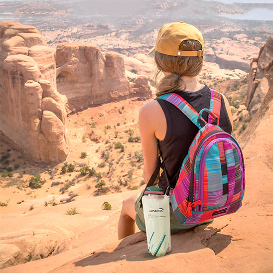 femme assise sur montagne et gourde pour le sport blanche posée à côté d elle