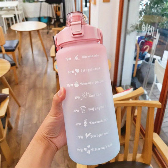 Gourde pour le sport rose et violette tenue à la main dans un café avec marqueur temporel visible