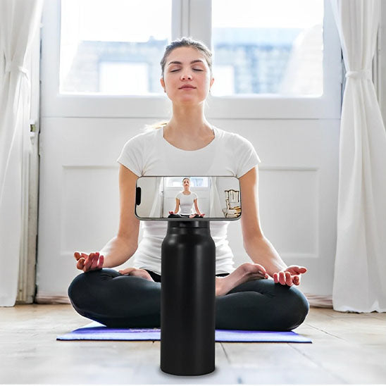 femme fait du yoga avec gourde sport noire et un telephone attaché à la gourde par aimant en face d elle