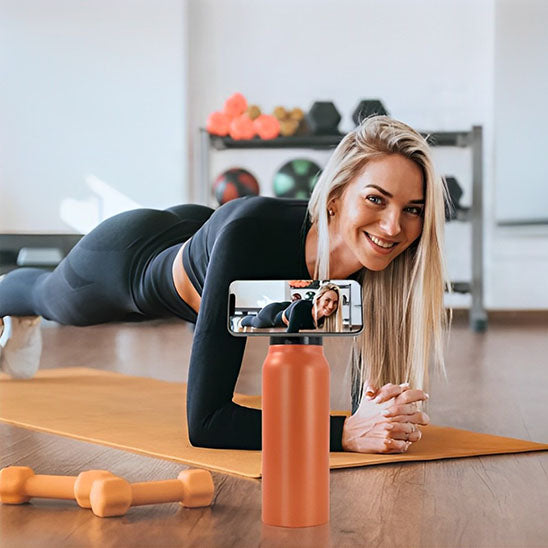 femme fait du fitness avec gourde sport orange et un telephone attaché à la gourde par aimant en face d elle