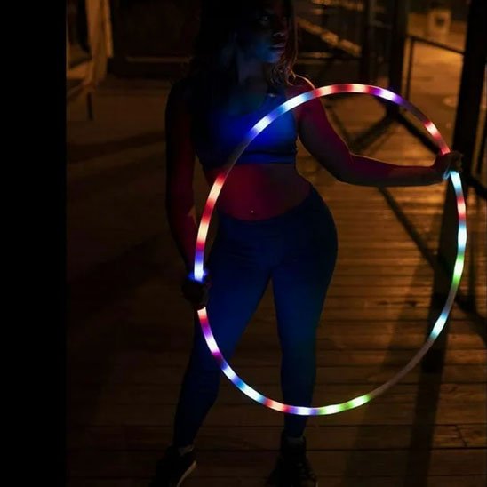 Hula hoop LED multicolore porté par une femme lors d’une séance fitness nocturne parfait pour allier sport et style