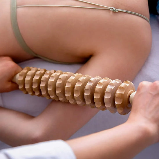 Femme massant ses bras avec un rouleau de massage en bois à 9 rouleaux allongée sur une table de soin