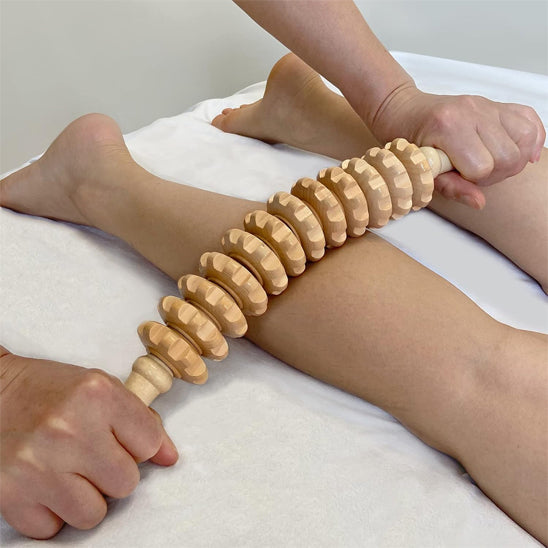 Application du rouleau de massage en bois sur les mollets pour améliorer la circulation et détendre les muscles