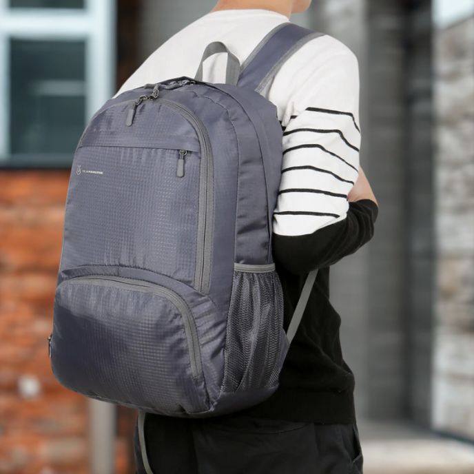 Sac a dos pour sport gris porté par une personne habillée de manière décontractée le sac est structuré avec plusieurs poches zippées