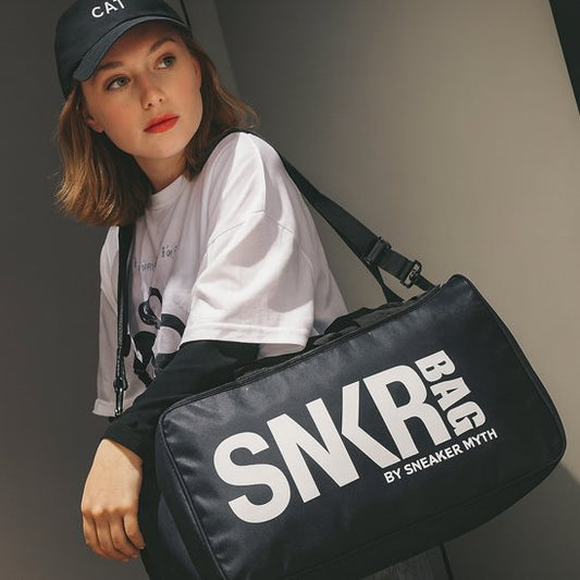 Jeune femme portant un sac de sport femme noir sur l épaule vêtue dun t-shirt blanc et d une casquette noire