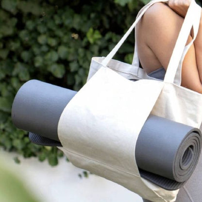 femme porte sac de sport femme beige sur son épaule avec tapis de yoga dans les manches latérales du sac