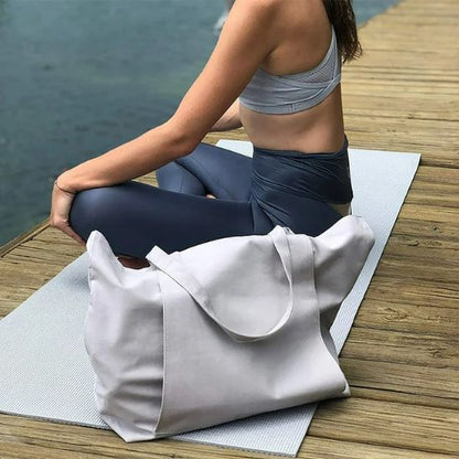 femme fait du yoga avec sac yoga beige a coté d elle au bord de la plage
