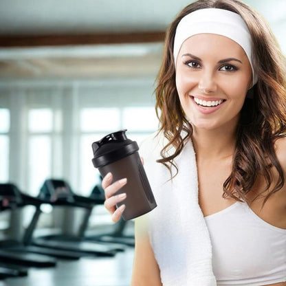 jeune femme en salle de sport tenant un shaker proteine noir et portant un bandeau blanc