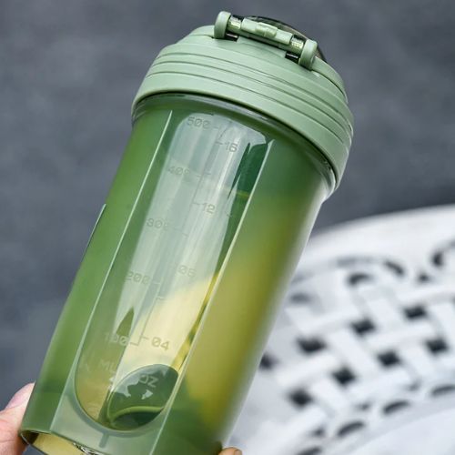 Shaker vert incliné tenu en main montrant la transparence du contenant et son compartiment intérieur