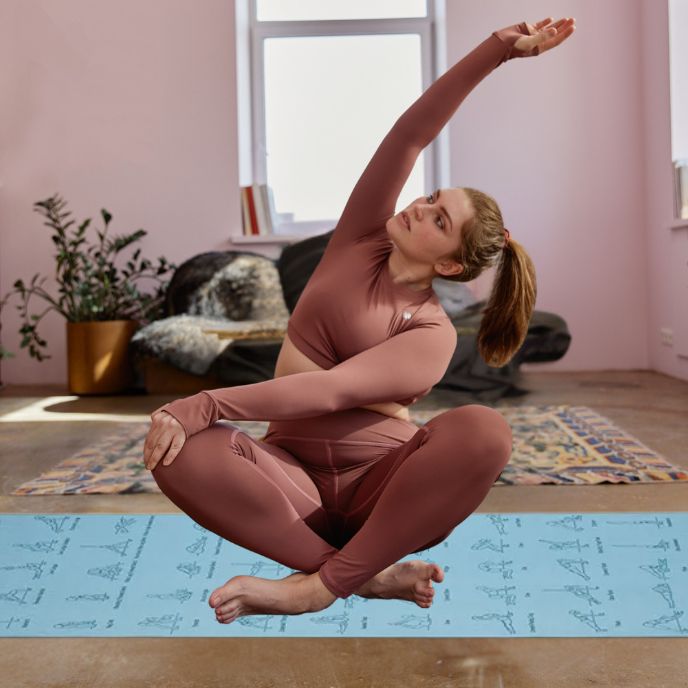 femme assise sur grand tapis yoga avec jambes croisées et bras vers le haut